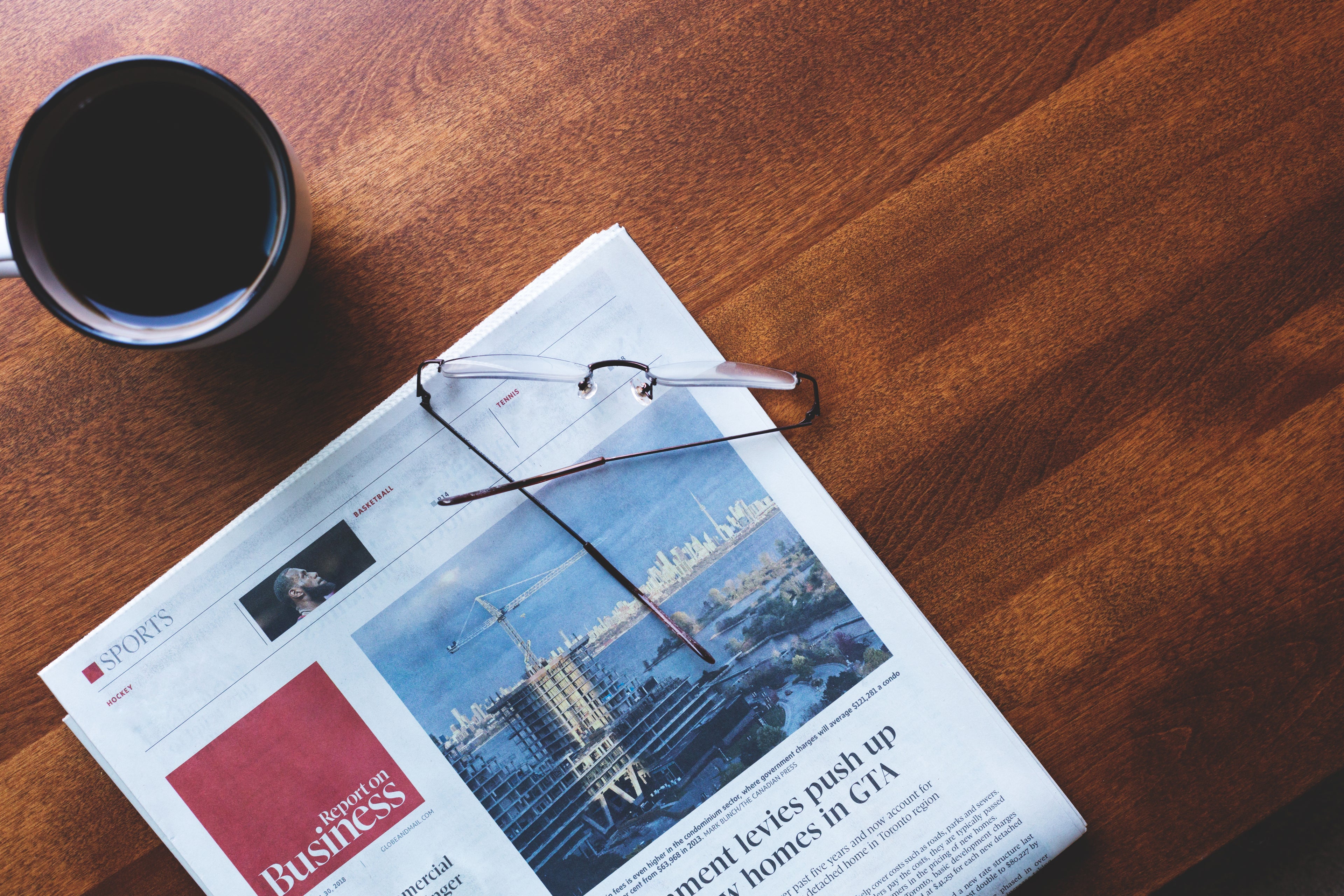 A coffee, newspaper, and glasses on a wooden table