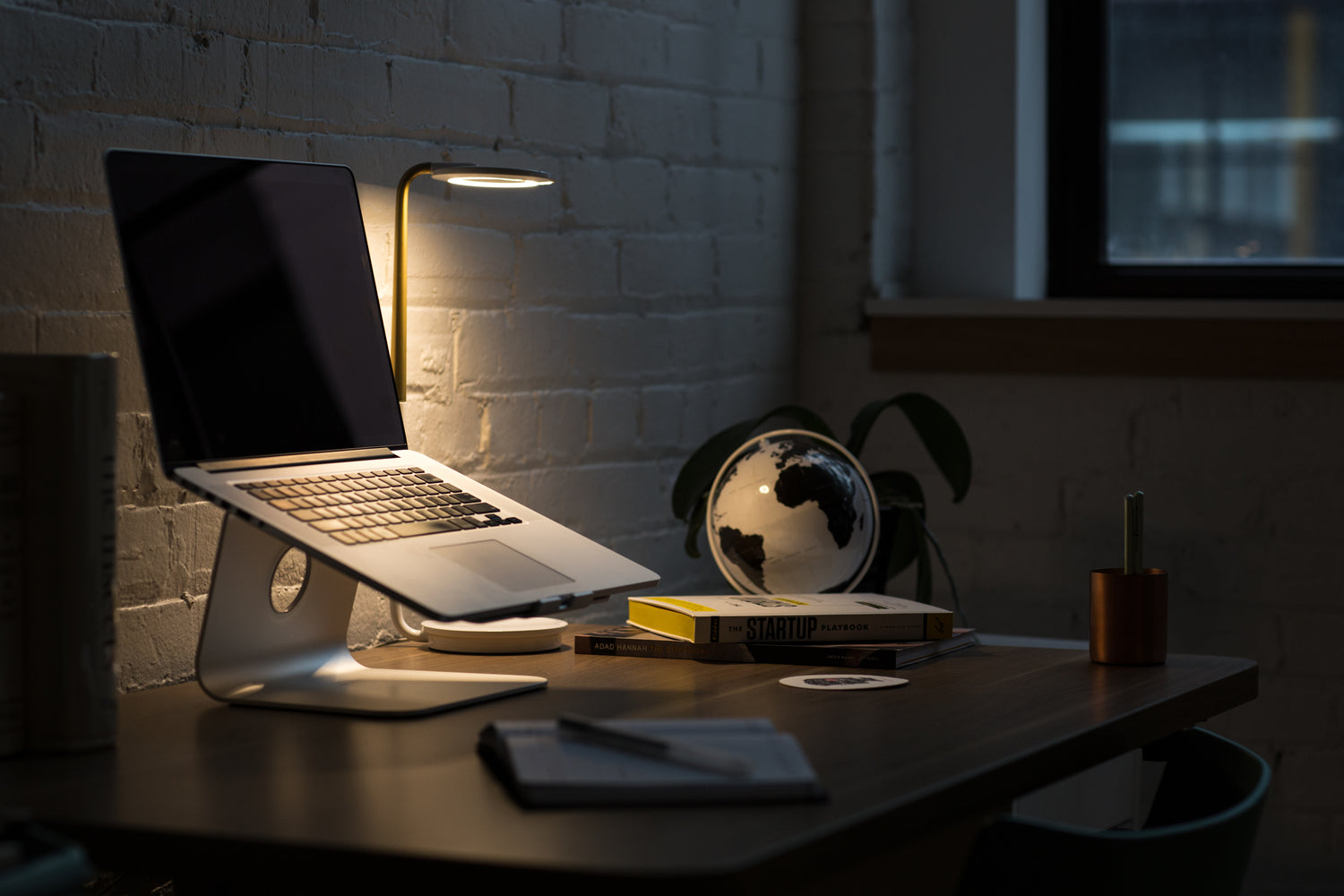 a desk with a laptop and books lit by a lamp